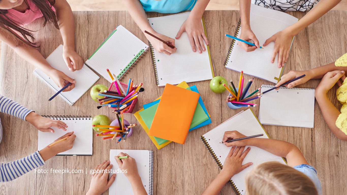 Schülerinnen sitzen an einem Tisch und lösen Aufgaben. Auf dem Tisch stehen Gläser mit Stiften.