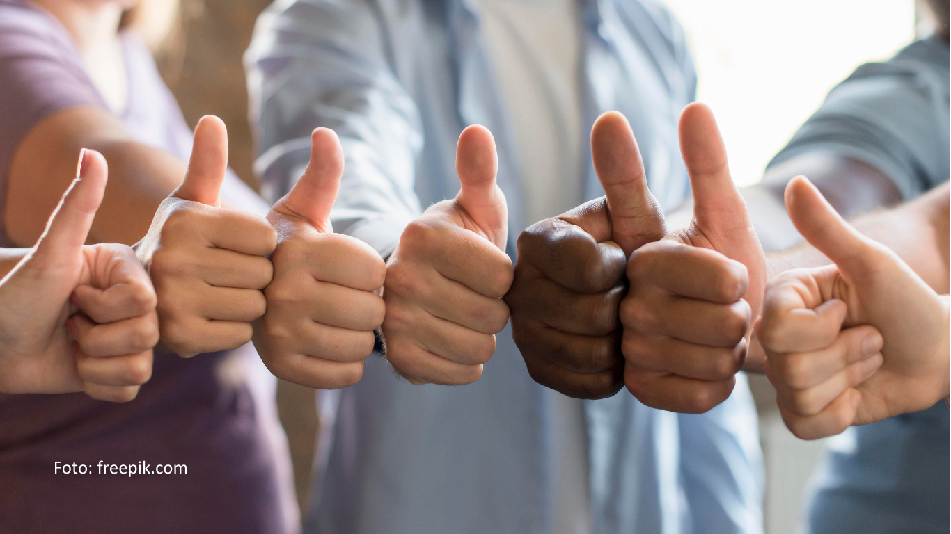 Eine diverse Gruppe von Menschen hält einen Daumen nach oben in die Kamera.