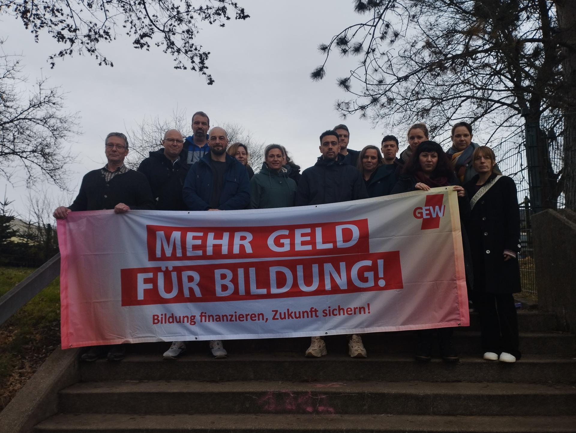 Ein Schreibtisch auf dem B&uuml;cher, Stifte und ein Globus steht. Im Hintergrund ist eine voll geschriebene Tafel.