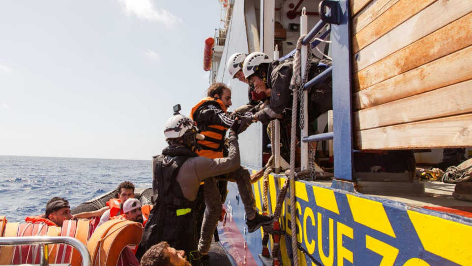 Menschen werden von einem kleinen Boot auf ein Sea-Watch-Boot gerettet.